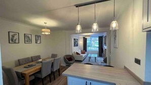 A modern kitchen with a central island, pendant lighting, and a dining area with a wooden table and chairs. - Charming Central Torquay Cottage (Torquay)