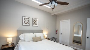 Un dormitorio ordenado con cama, lámparas de noche, ventilador de techo y una puerta con espejo.