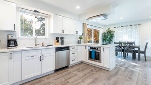 Une cuisine moderne avec des meubles blancs, un lave-vaisselle, un four et un coin repas comprenant une table et des chaises.