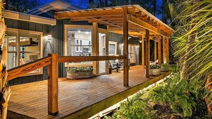 Een modern huis met een houten terras, grote ramen en een overdekte patio.