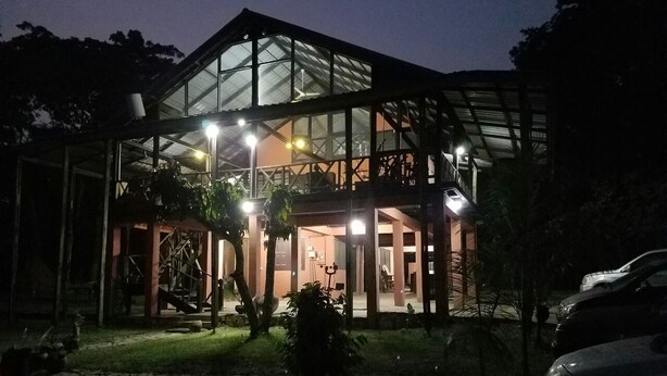 A modern building with a glass facade and a covered outdoor area, illuminated by multiple lights. - Cosy, personal, family-friendly nature retreat surrounded by trees and fresh air (Aburi)