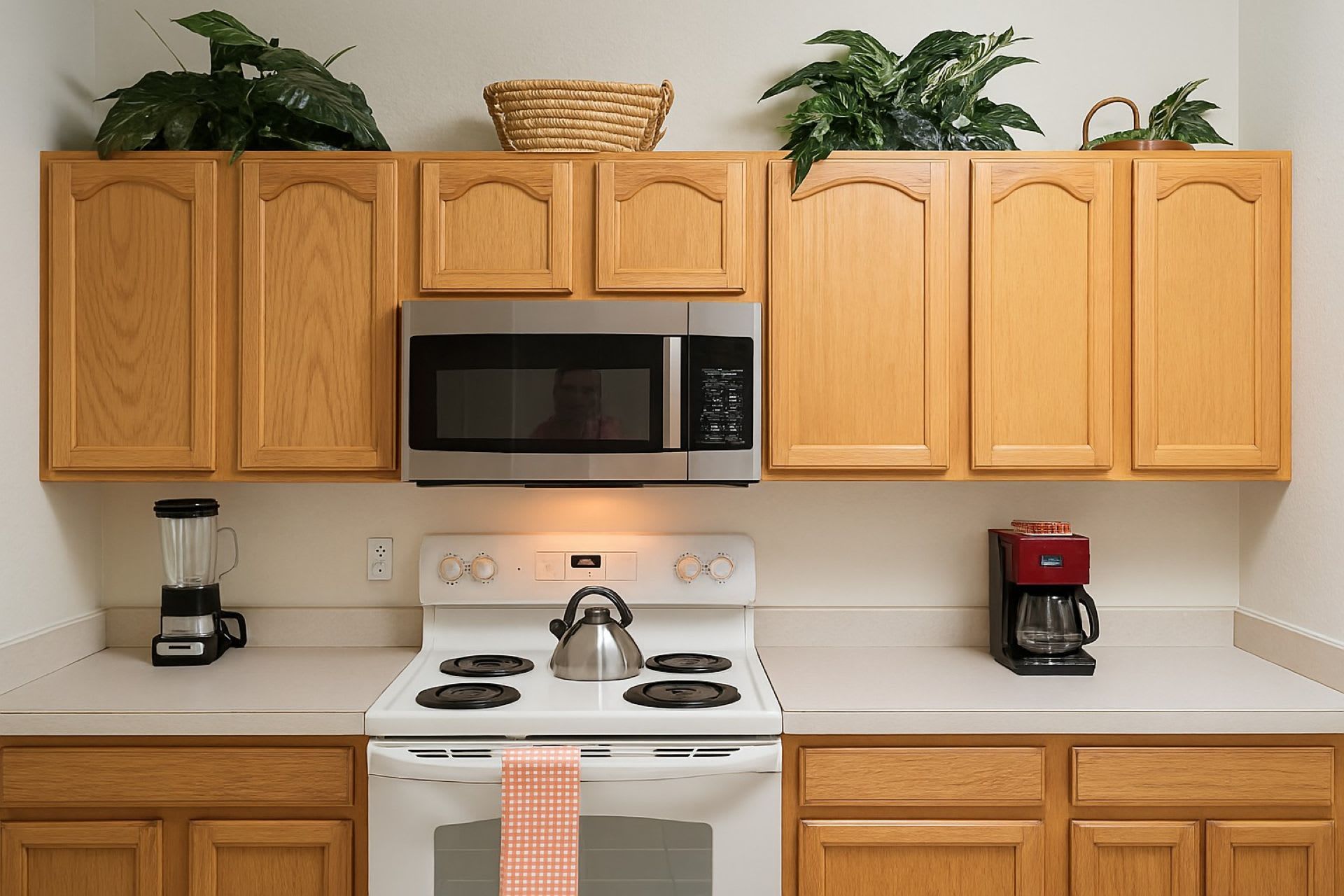 Una cocina con armarios de madera, un microondas de acero inoxidable, una estufa blanca, una cafetera y una licuadora.