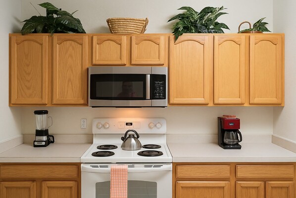 A kitchen with wooden cabinets, a stainless steel microwave, a white stove, a coffee maker, and a blender.
