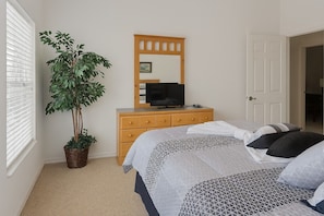 A bedroom with a bed, a dresser, a television, and a potted plant.