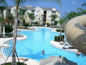 A swimming pool with a water slide, palm trees, and a multi-story building in the background. - Disney 10-Min Drive! Resort Condo w/ Pool & (Kissimmee)