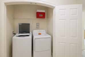 A laundry room with a washer and dryer, a red storage box, and a shelf above the dryer.