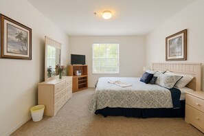 Ein Schlafzimmer mit Bett, Kommode, Fernseher und Fenster.