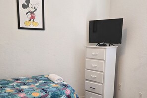 A bedroom with a bed, a TV on a stand, a dresser, and a Mickey Mouse poster on the wall.