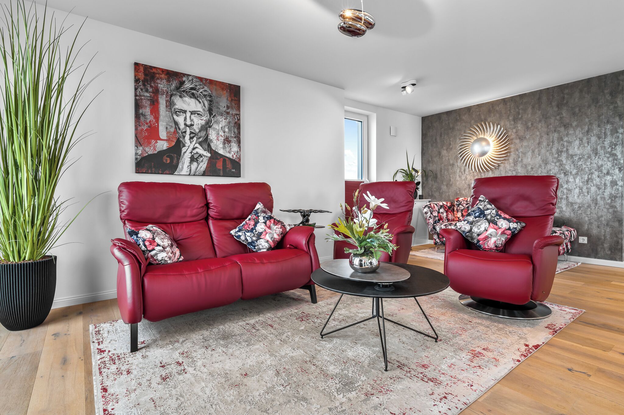 Ein modernes Wohnzimmer mit zwei roten Ledersofas, einem runden Couchtisch und einer großen Topfpflanze.