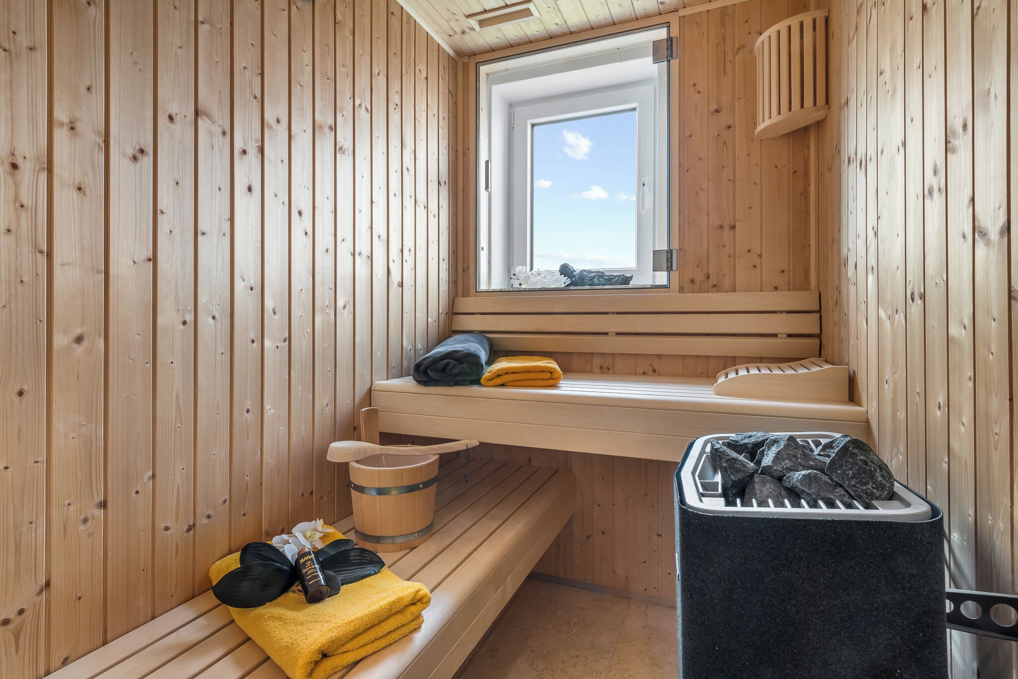 A sauna room with wooden walls, a bench, a window, and a stone basin.