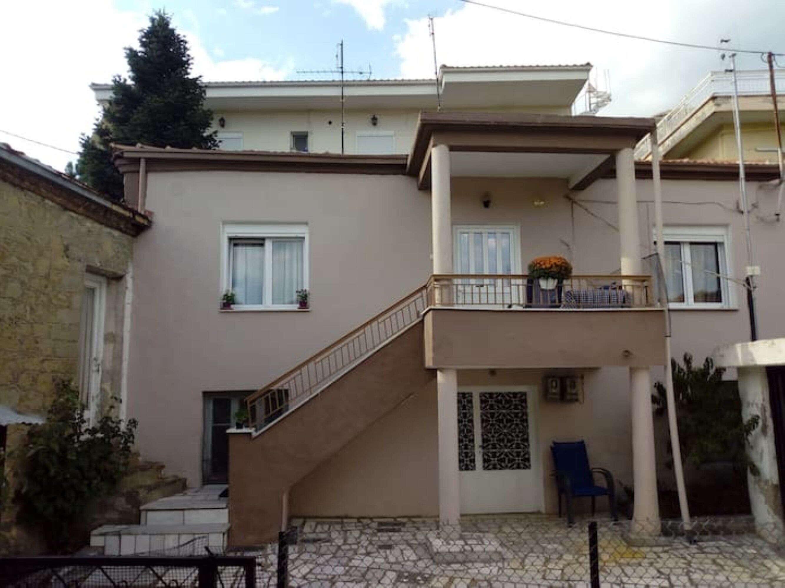 Un bâtiment à deux étages doté d’un balcon, d’un escalier et d’une porte ornée d’une grille décorative.