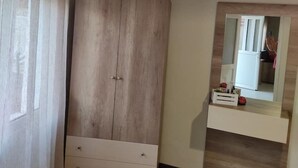Un dormitorio con un armario de madera, un espejo sobre un tocador y una ventana con cortinas.