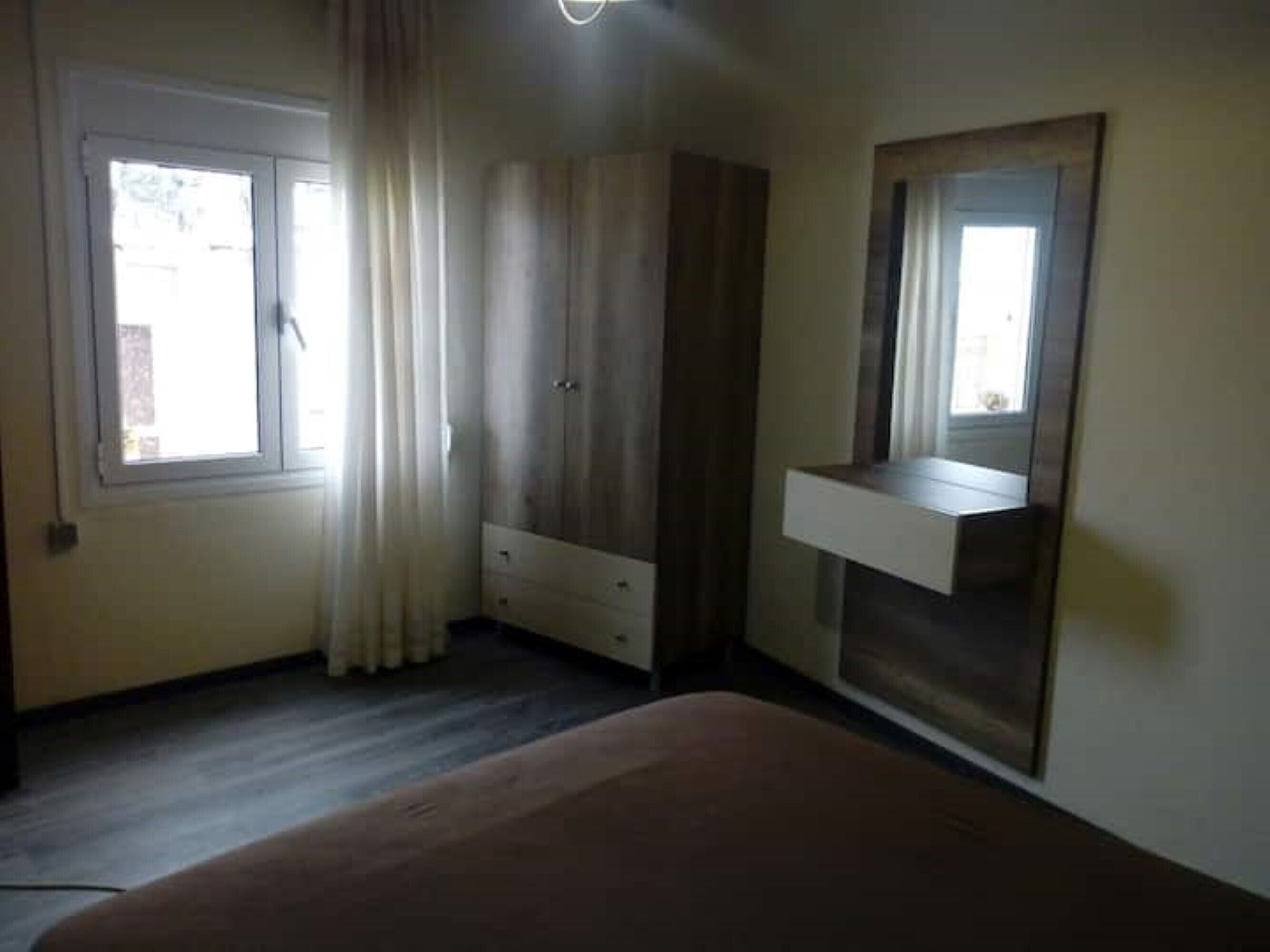 A bedroom with a bed, a wardrobe, a mirror, and a window with curtains.