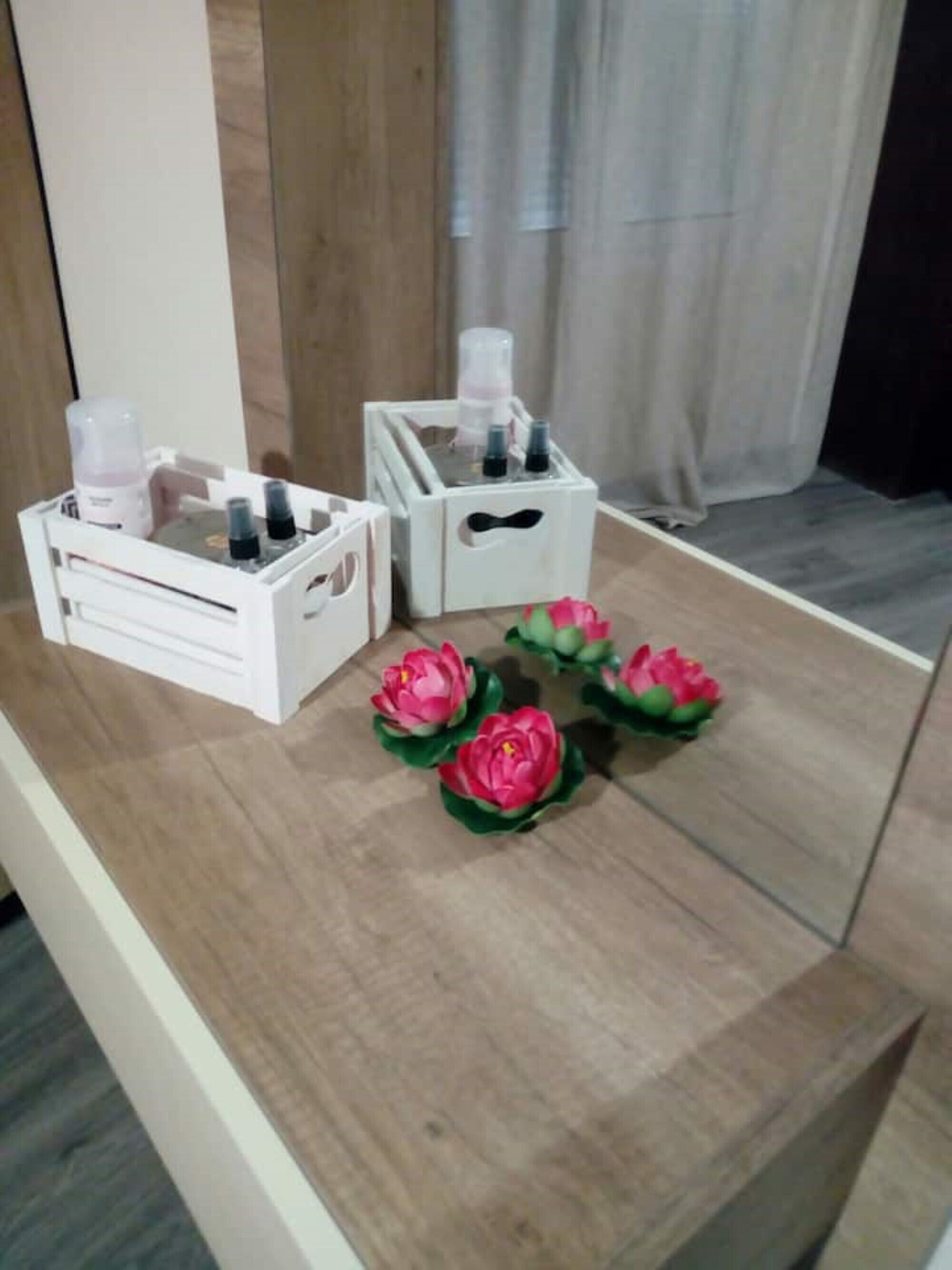 A wooden table with white storage boxes and pink artificial flowers.