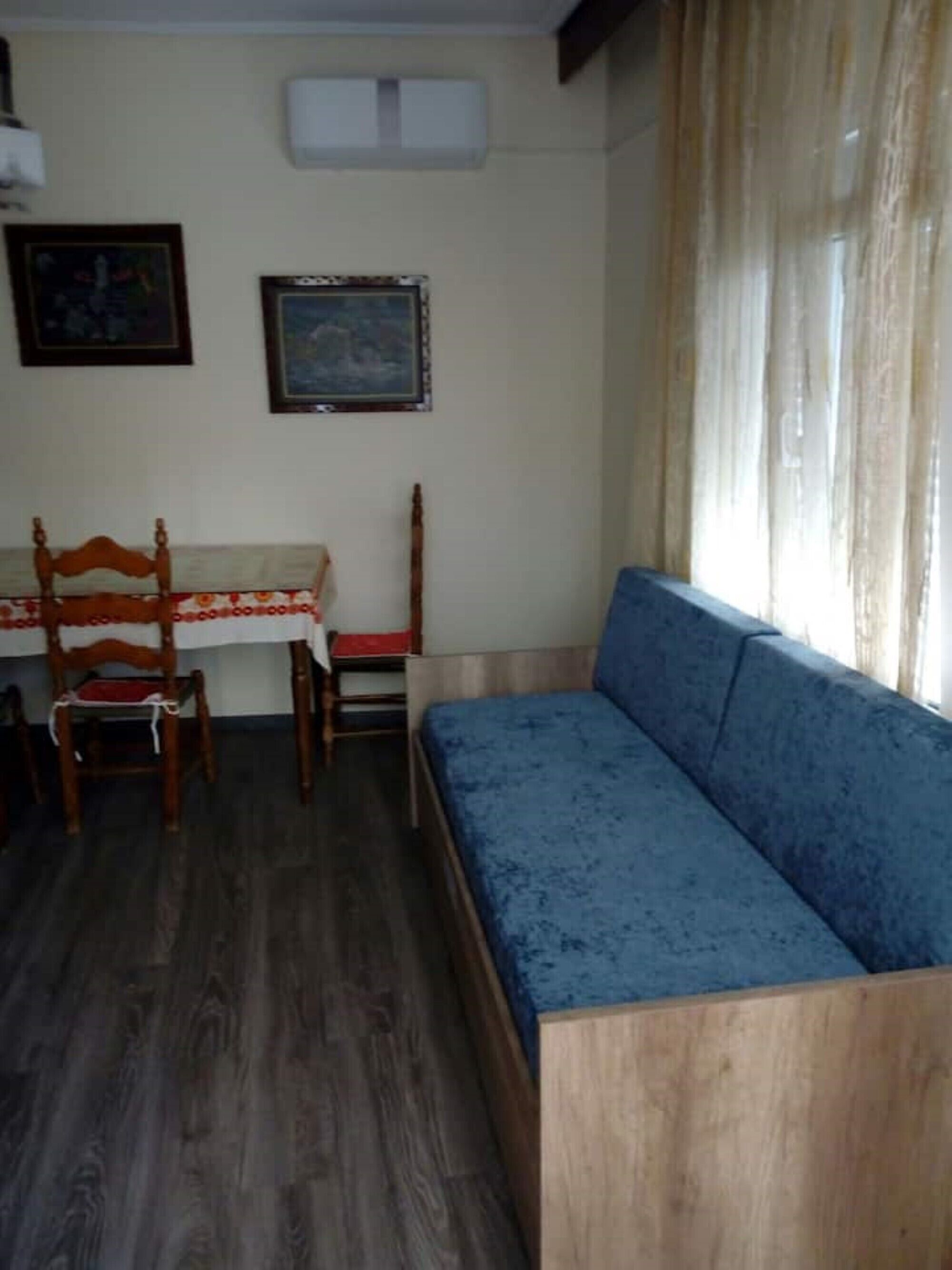 A room with a blue sofa, wooden chairs, a table with a red and white tablecloth, and two framed pictures on the wall.