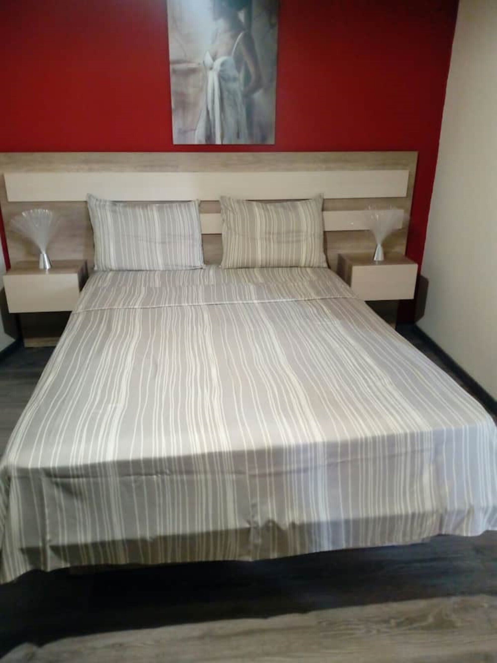 A bed with a striped bedspread, two pillows, and a headboard. There are two bedside tables with lamps on either side of the bed.