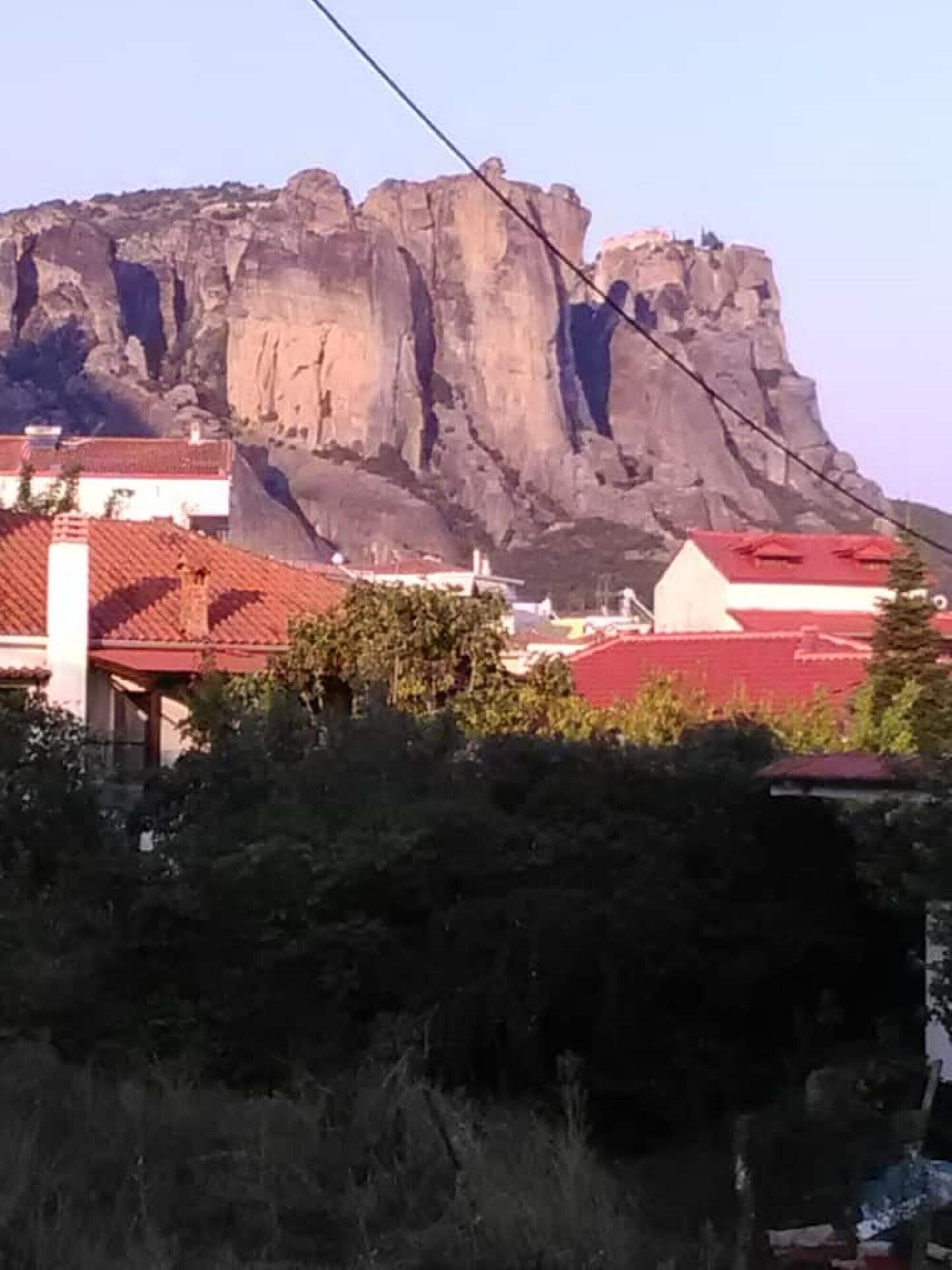 A mountain with a rocky face and a few buildings with red roofs in the foreground.