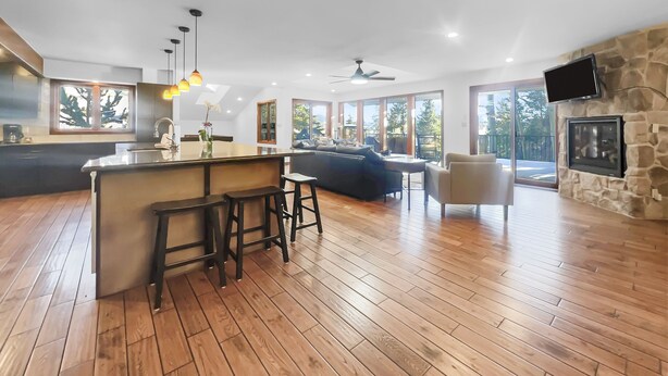 Un vaste espace de vie doté d’un plancher en bois, d’un îlot central avec des tabourets, d’un canapé et d’un téléviseur fixé à un mur en pierre.