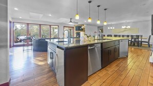Une cuisine moderne dotée d’un îlot central, de planchers en bois, de luminaires suspendus et d’un coin repas avec des chaises et une table.