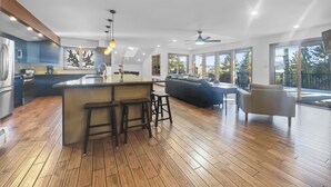 Une cuisine moderne dotée d’un îlot central, de planchers en bois et de grandes fenêtres offrant une vue sur l’extérieur.