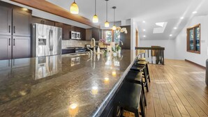Une cuisine moderne dotée d’un grand îlot central, d’appareils électroménagers en acier inoxydable et de luminaires suspendus.