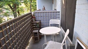 A small outdoor patio with a table and chairs, a wooden stool, and a lattice fence. - I10 - Apt|Patio|11mi to Convention Ctr|Sleeps 2 (Irving)