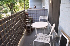 Eine kleine Terrasse im Freien mit Tisch und Stühlen, einem Holzschemel und einem Spalierzaun.