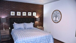 Quarto com cama, mesas de cabeceira, parede de tijolos e uma decoração na parede.