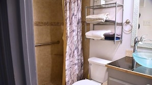 A bathroom with a shower, toilet, and a sink with a glass basin. - I10 - Apt|Patio|11mi to Convention Ctr|Sleeps 2 (Irving)