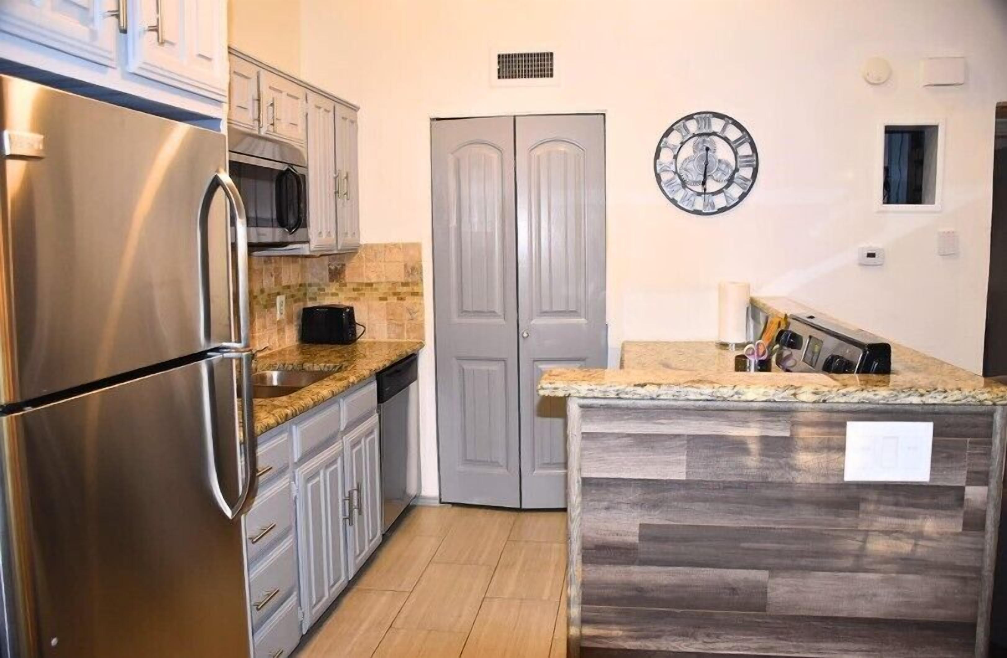 A kitchen with a stainless steel refrigerator, microwave, and granite countertop.