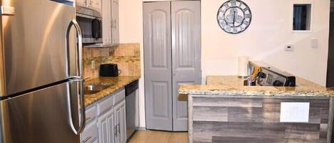 Una cocina con refrigerador de acero inoxidable, microondas y encimera de granito.
