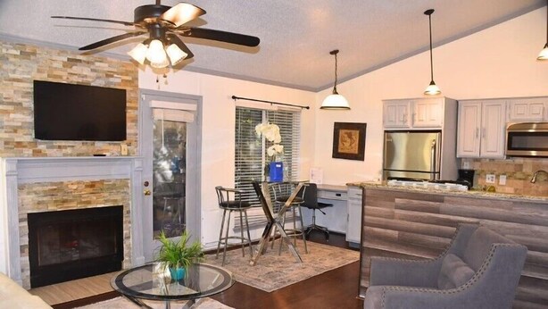 A living room with a fireplace, a dining area with chairs, a kitchen with cabinets and appliances, and a ceiling fan. - I10 - Apt|Patio|11mi to Convention Ctr|Sleeps 2 (Irving)