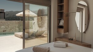 A modern bedroom with a large bed, a bathroom with a mirror, and a balcony with a view of mountains. - Increteblue Suites (Agios Vasileios)