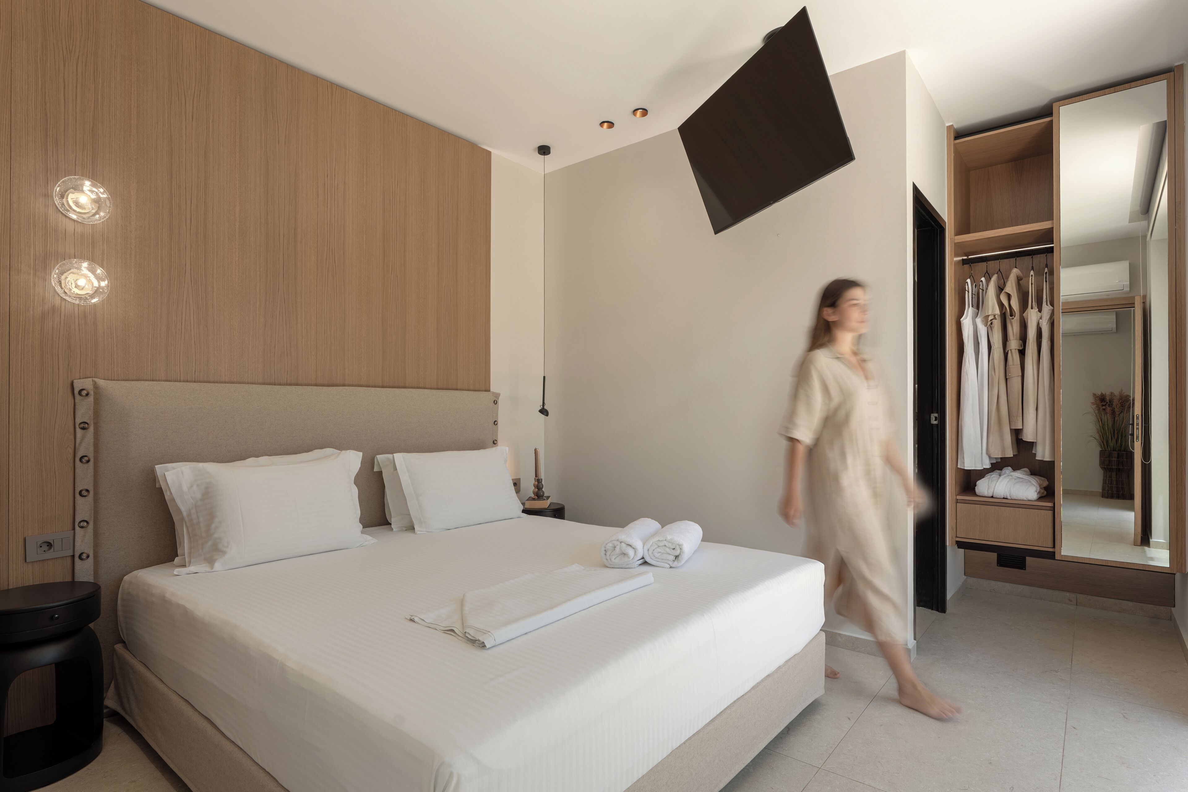 A modern hotel room with a large bed, a wardrobe, a flat-screen TV, and a bedside table.