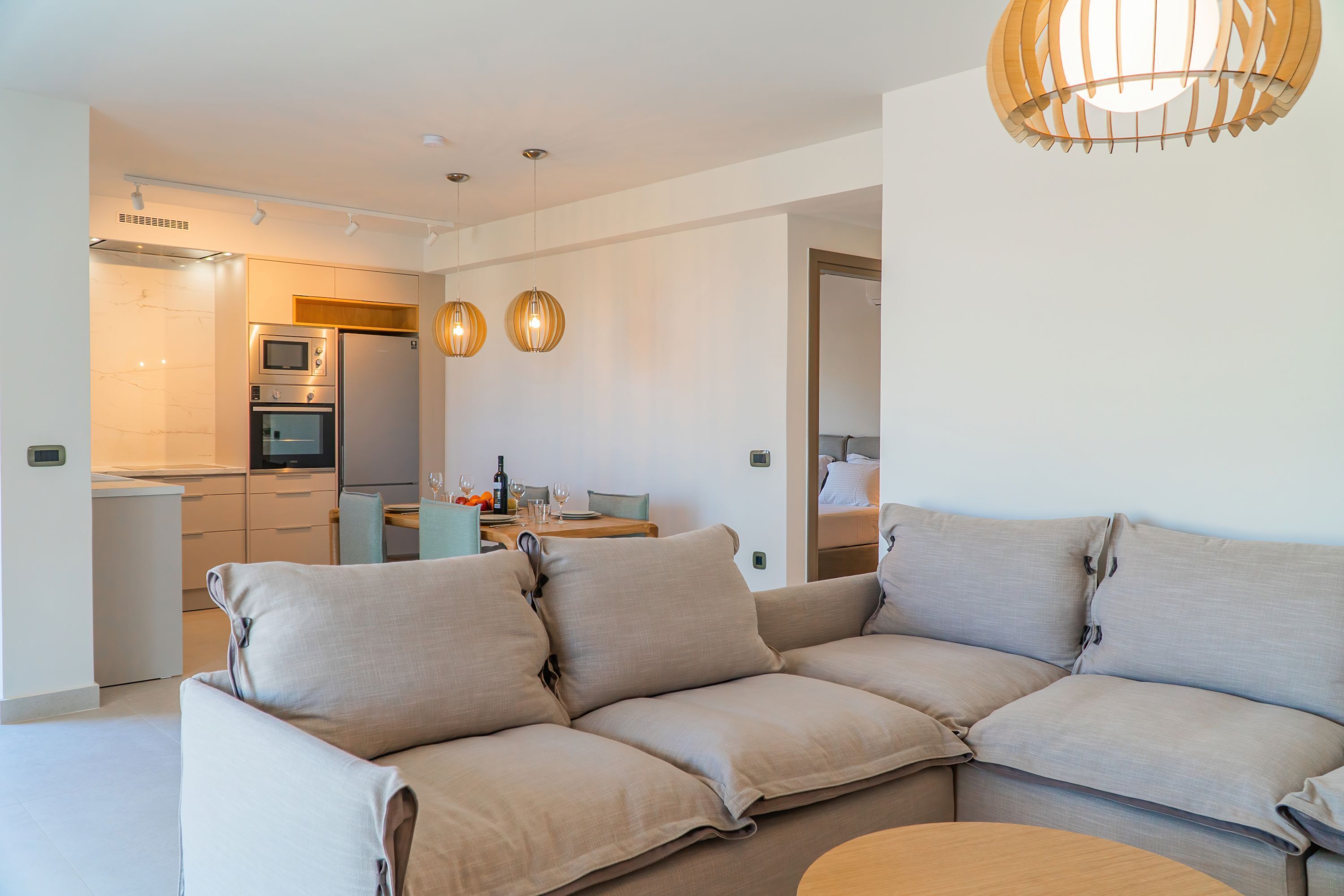Una sala moderna con un sofá seccional color beige, una mesa de centro de madera e iluminación colgante.