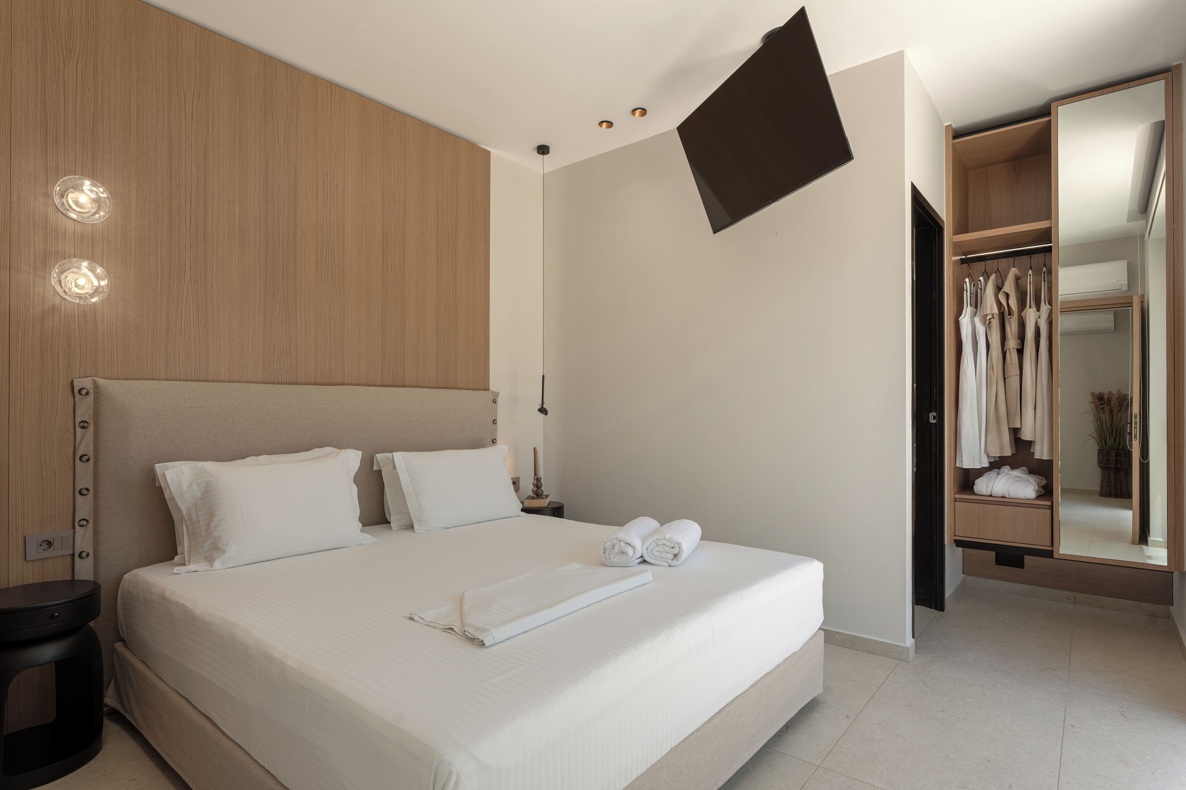 Une chambre d’hôtel moderne dotée d’un grand lit, d’un téléviseur à écran plat fixé au mur, d’un dressing et d’une table de chevet.
