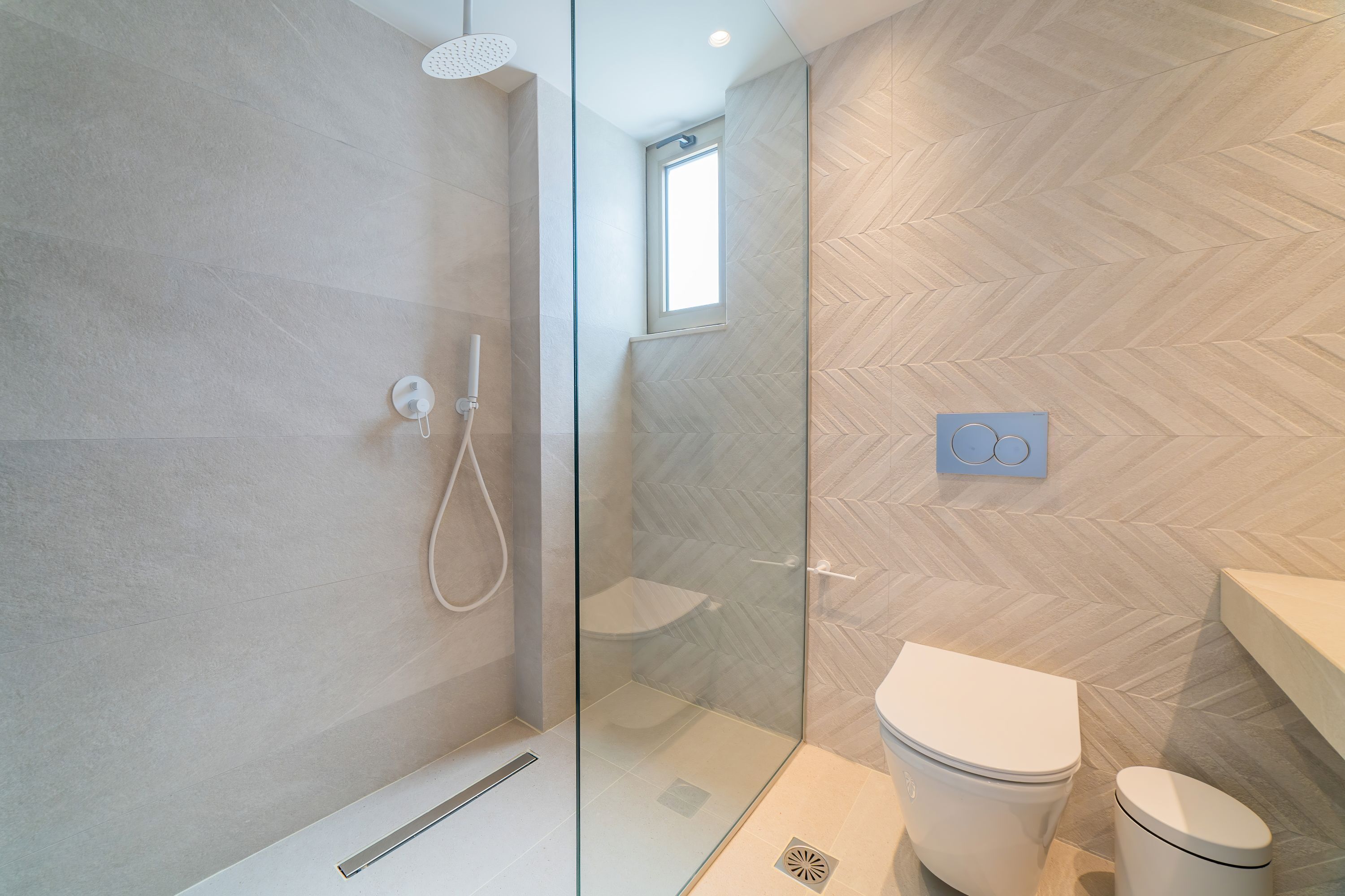 A modern bathroom with a glass-enclosed shower, a toilet, and a herringbone-patterned floor.