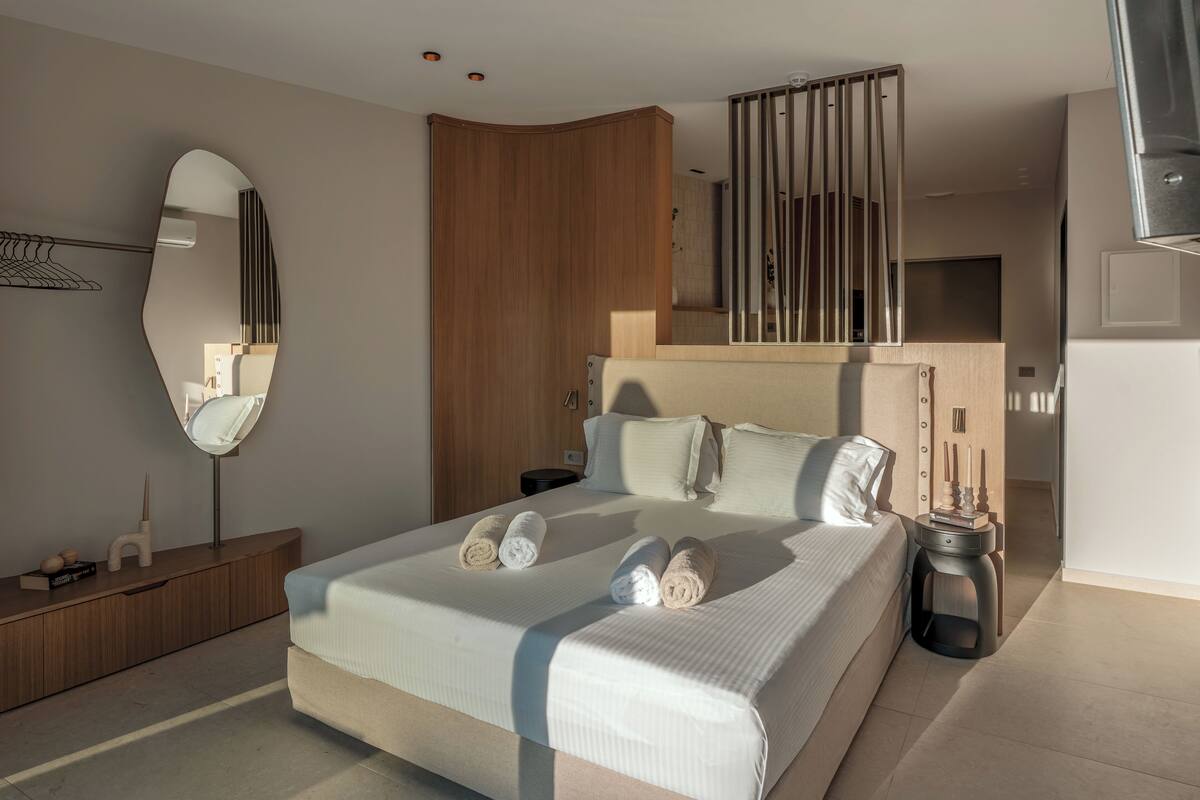 A modern bedroom with a large bed, a wooden wardrobe, a mirror, and a nightstand.