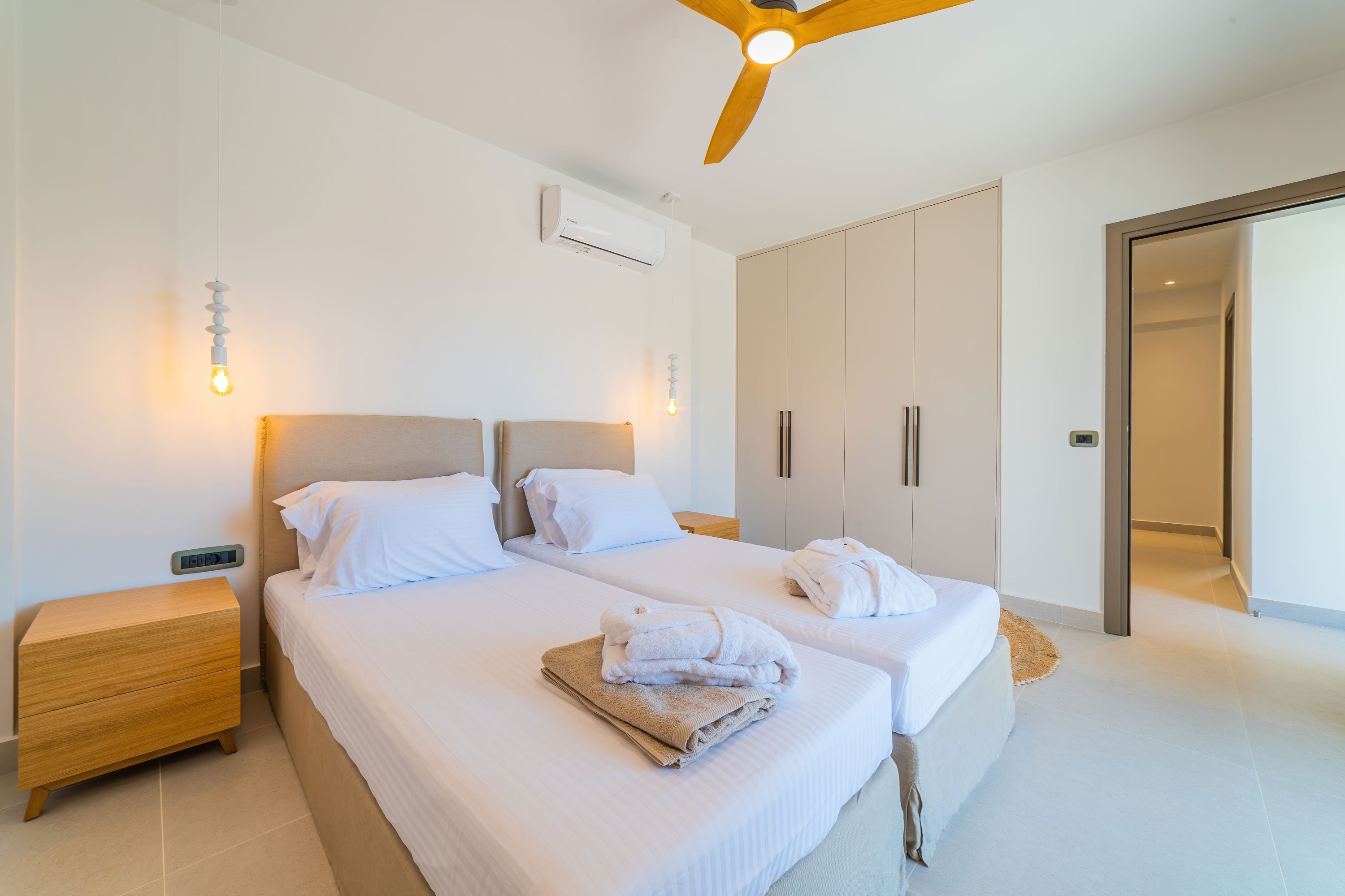Ein modernes Schlafzimmer mit zwei Betten, einem Deckenventilator, einer Klimaanlage und einem Nachttisch aus Holz.