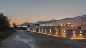 A paved driveway leading to a modern building with stone walls and exterior lighting. - Increteblue Suites (Agios Vasileios)