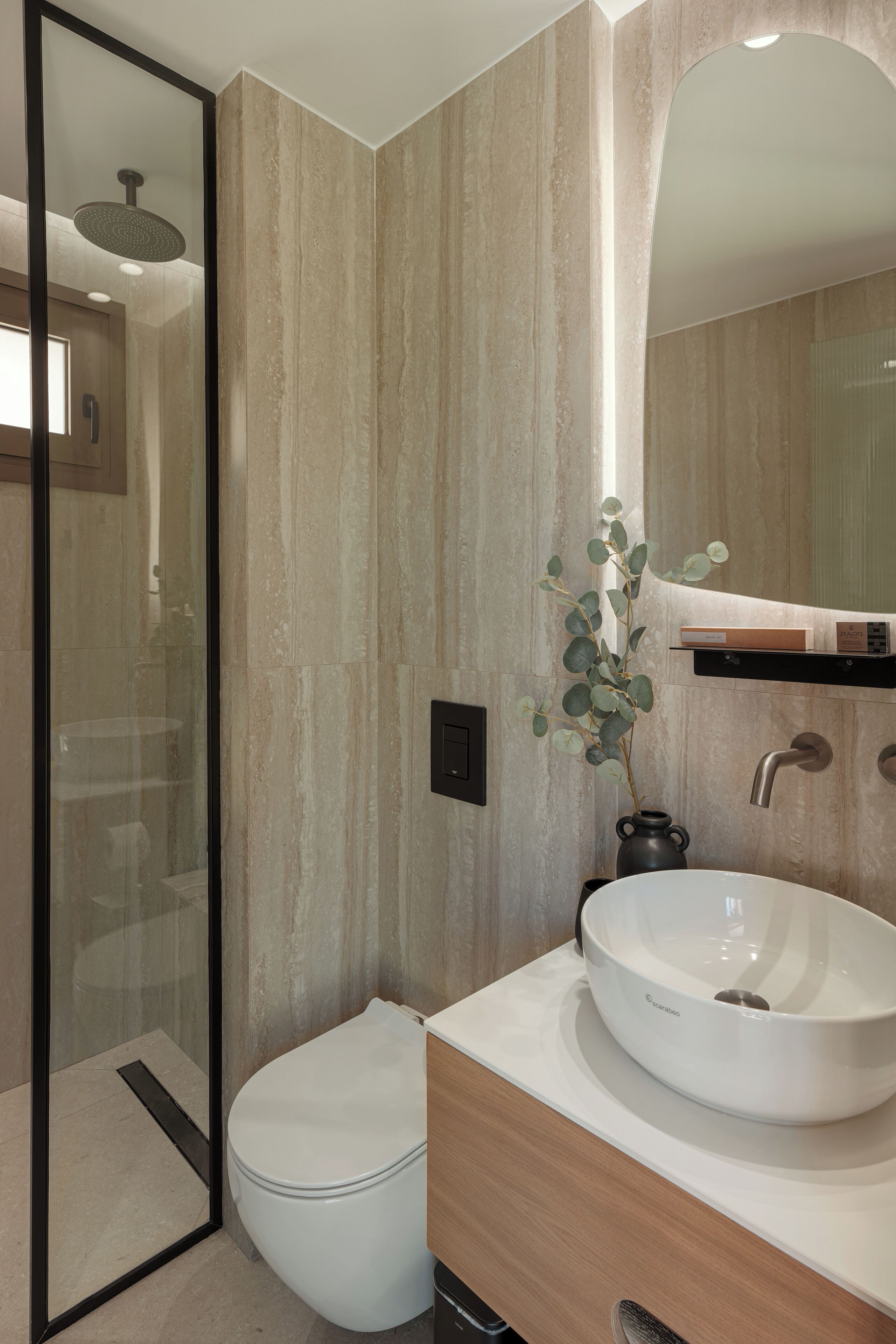 A modern bathroom with a glass shower enclosure, a white toilet, a white sink with a vessel, and a mirror above the sink.
