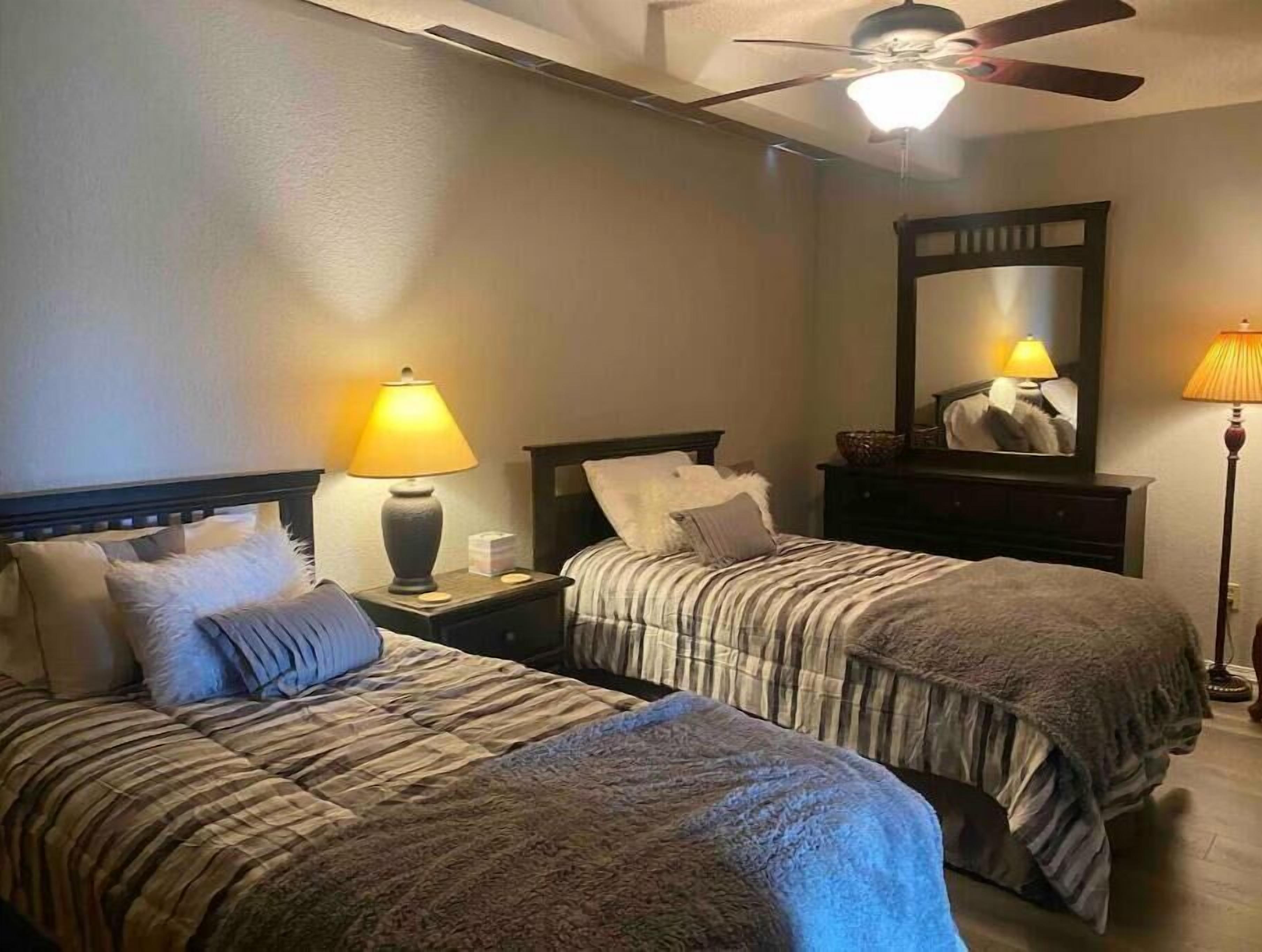 Une chambre d’hôtel avec deux lits, un ventilateur de plafond, un miroir et une table de chevet avec une lampe.