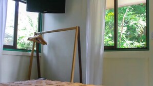 Quarto com cama, cabide de madeira e janela com vista para o verde.