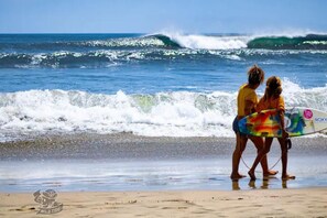 Ein Strand mit Wellen und zwei Personen, die ein Surfbrett tragen.