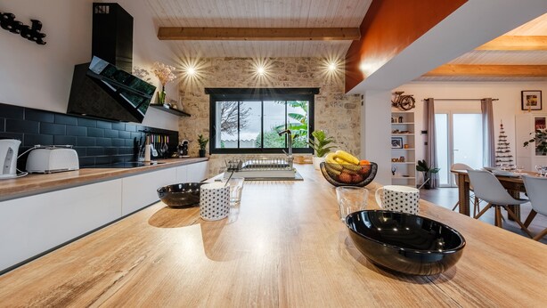 A modern kitchen with a wooden countertop, black appliances, and a large window.