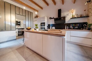 A modern kitchen with white cabinetry, a wooden countertop, and a black backsplash. There is a built-in oven and a coffee machine on the counter.