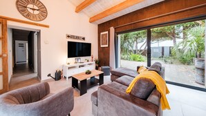 A modern living room with a large TV, comfortable seating, and a view of the outdoors.