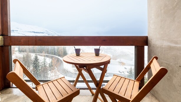 Uma mesa de madeira e duas cadeiras em um quarto com vista para uma paisagem nevada.