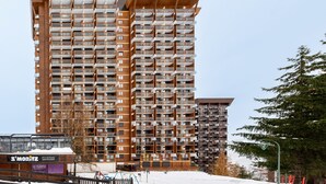 Um edifício alto com várias varandas, um restaurante chamado "3'MORITZ" na base e um ambiente coberto de neve.