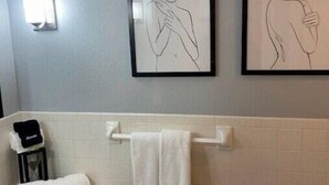Ein Badezimmer mit einem weißen Waschbecken, einem Handtuchhalter mit zwei Handtüchern und zwei gerahmten Linienzeichnungen an der Wand.